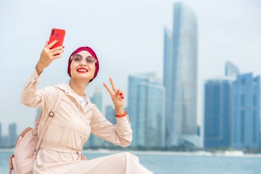 Su berrakken ve arka planda Abu Dabi 'nin gökdelenleri yükselirken genç bir kadın sahilde selfie çekerek anı ve çarpıcı manzarayı yakalıyor..
