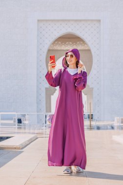 Geleneksel Abaya kıyafetleri içinde genç bir turist kız hac yolculuğunu Şeyh Zayed Büyük Camii 'nden selfie ile belgeliyor..