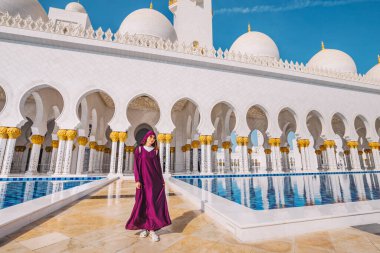 Geleneksel Arap abaya elbiseli bir kız, Abu Dabi, BAE 'deki ünlü Şeyh Zayed Camii' ndeki güzel bir havuzda ritmik sütunların ve yansımalarının arasında yürüyor.