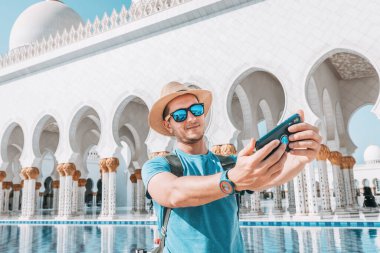 Sırt çantalı bir turist Abu Dabi 'deki Şeyh Zayed' in Büyük Camii 'nde selfie çekmek için cep telefonu kullanıyor.