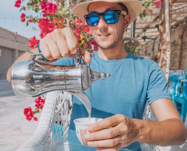 Dubai 'deki otantik bir Arap kafesinde, bir adam kendine geleneksel bir kahve demliğinden bir fincan mis kokulu kahve doldurur, biranın zengin lezzetinin ve aromasının tadını çıkarır..