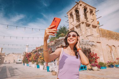 Akıllı telefonu elinde, mutlu bir turist kızı, Dubai 'den gelen takipçileriyle paylaşmak için bir selfie çekiyor..