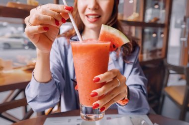 Bir kız bir kafede kamışla karpuz suyu içiyor.