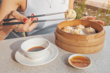 Çubuklu kız lezzetli, geleneksel Çin yemeği yiyor Xiao long bao köftesi ya da bambu tabağında sunulan baozi çörekleri otantik bir dokunuş için soya sosu..