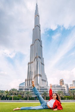 Mutlu komik kız çimenlerde uzanıyor ve Dubai, BAE 'deki görkemli Burj Halife kulesini seyrediyor.