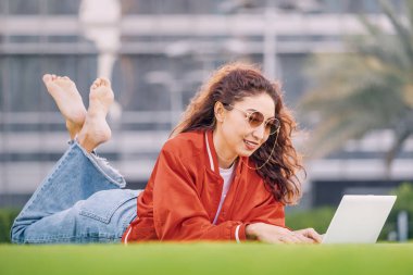 Parkın yeşil çimenleri mükemmel bir zemin oluşturuyor. Öğrenci bir kız laptopuna dikkatle odaklanıyor. Gün ışığını emerken daktilo yazıyor..