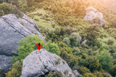 Uçurumun tepesinde kırmızı elbiseli bir kızın romantik hava fotoğrafı bir dağ geçidi manzarasına hayran.