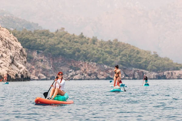 view of a group or team with paddles swims on a SUP boards on the sea near scenic rocks. Healthy lifestyle and recreation concept