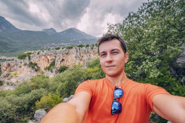 Mutlu yürüyüşçü ya da dağcı arka planda ünlü Geyikbayiri kayaları ve kanyonu olan bir patikada selfie çekerken.