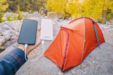 Akıllı telefon ve diğer elektrikli cihazları hafta sonu yürüyüşü sırasında şarj etmek için Powerbank. Arka planda turuncu kamp çadırı