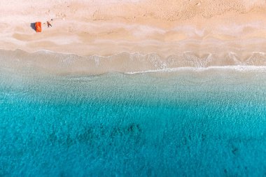 From above, the beauty of a beach unfolds, featuring a camping tent that stands as a humble sanctuary amidst the vast coastal expanse.