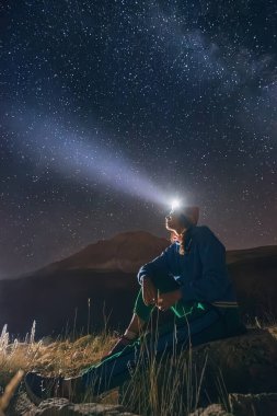 Yıldızlı gece gökyüzünün altında, bir kız el feneriyle keşfeder, dağ manzarasına biraz macera katar..