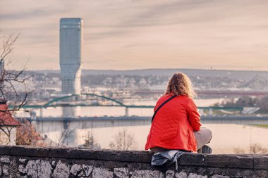 02 Ocak 2024, Belgrad, Sırbistan: Belgrad 'ın ufuk çizgisinin cazibesi gün batımında, genç bir kadının bir tepenin tepesinden kentsel cazibeyle doğal güzelliği harmanladığı şehir manzarasına baktığı yerde.