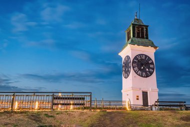 Petrovaradin Kalesi 'nin ikonik saat kulesi Novi Sad üzerinde güneş batarken, Sırp tarihi ve kültürünün pitoresk bir manzarasını sunuyor..