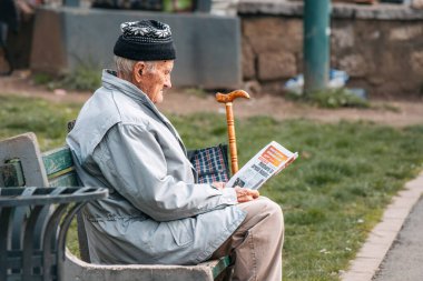 15 Mart 2024, Saraybosna, Bosna-Hersek: Bir bankta oturan yaşlı beyefendi, ciddi ama yine de içerik bir ifadeyle gazeteye daldı.