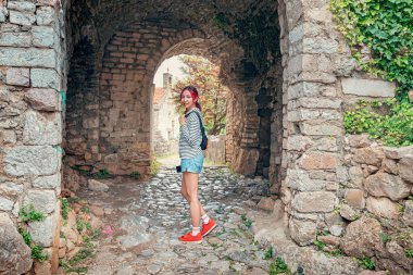 Karadağ 'ın eski Bar kentindeki taş kemer yolunun önünde bir gezgin kadın duruyor. Çizgili bir gömlek ve şort giyiyor.
