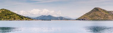 Önünde Skadar gölü olan güzel bir dağ sırası. Gökyüzü turuncu ve pembe renklerin karışımıdır. Huzurlu ve huzurlu bir atmosfer yaratır.