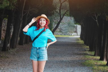 Şık şapkalı genç bir kadın, ağaçlarla ve ara sokaklarla çevrili bir yaz gününün tadını çıkarıyor..