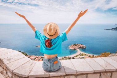 Karadağ 'da gezgin bir kadın, Sveti Stefan ve kıyı dağlarının panoramik manzarasıyla lüks bir tatilin tadını çıkarıyor.