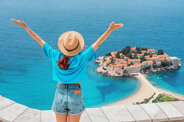 Karadağ 'da gezgin bir kadın, Sveti Stefan ve kıyı dağlarının panoramik manzarasıyla lüks bir tatilin tadını çıkarıyor.