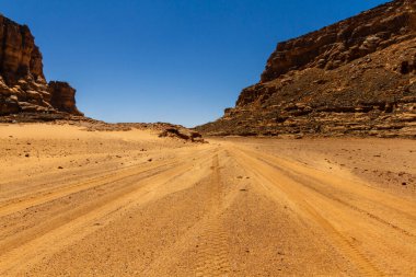 Empty sandy dirt road with tire tracks in Tassili National Park. Tadrart mountains, Acacus range. Tassili N'Ajjer National Park. Algeria, Africa  