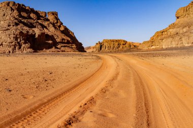 Tassili Ulusal Parkı 'nda tekerlek izleri olan boş kumlu bir yol. Tadrart Dağları, Acacus Dağları. Tassili N 'Ajjer Ulusal Parkı. Cezayir, Afrika  