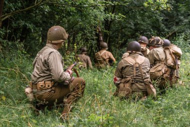 2. Dünya Savaşı sırasında Amerikan piyade askeri gibi giyinmiş tarihi reeneaktörler ormanda devriye geziyor. Arkadan bak. Porbka, Polonya