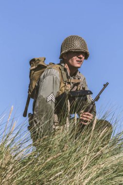 2. Dünya Savaşı dönemi piyade askeri gibi giyinmiş tarihi yeniden canlandırmacı, tarihi bir canlandırma sırasında uzun otların arasında diz çökerken bölgeye bakıyor. İmdat, Polonya