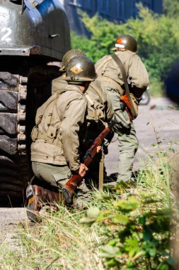 Tarihi yeniden yapılandırma. 2. Dünya Savaşı 'ndan kalma bir Amerikan piyade askeri bir tankın arkasına saklanarak saldırmaya hazırlanıyor. Arkadan bak..