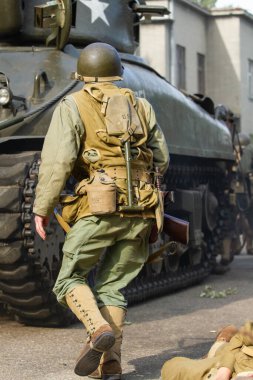 Tarihi yeniden yapılandırma. 2. Dünya Savaşı 'ndan kalma bir Amerikan piyade askeri bir tankın arkasına saklanarak saldırmaya hazırlanıyor. Arkadan bak..