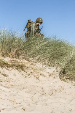 2. Dünya Savaşı dönemi piyade askeri gibi giyinmiş tarihi yeniden yapılandırma uzmanı, uzun otların arasında diz çökerken bölgeyi izliyor. 