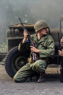 Tarihi yeniden yapılandırma. 2. Dünya Savaşı 'ndan kalma bir Amerikan piyade askeri, askeri bir aracın arkasına saklanarak saldırmaya hazırlanıyor..