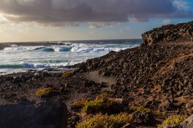 Güneş batarken Atlantik kıyısındaki siyah volkanik kayalar. Playa de las Malvas, Lanzarote, Kanarya Adaları, İspanya