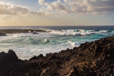 Güneş batarken Atlantik kıyısındaki siyah volkanik kayalar. Playa de las Malvas, Lanzarote, Kanarya Adaları, İspanya