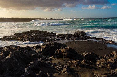 Black volcanic rocks on the Atlantic coast at sunset. Playa de las Malvas, Lanzarote, Canary Islands, Spain clipart