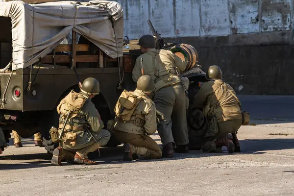 Tarihi yeniden yapılandırma. 2. Dünya Savaşı 'ndan kalma Amerikan piyade askerleri askeri bir aracın arkasına saklanarak saldırmaya hazırlanıyor. Arkadan bak.
