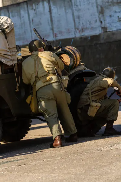 Tarihi yeniden yapılandırma. 2. Dünya Savaşı 'ndan kalma Amerikan piyade askerleri askeri bir aracın arkasına saklanarak saldırmaya hazırlanıyor. Arkadan bak.