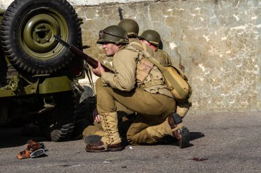 Tarihi yeniden yapılandırma. 2. Dünya Savaşı 'ndan kalma bir Amerikan piyade askeri, askeri bir aracın arkasına saklanarak saldırıya geçmeye hazırlanıyor.
