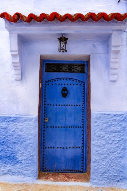 Şehir mimarisi. Geleneksel mavi ahşap kapı, yuvarlak demir tokmaklı ve çivili. İslami motif. Şef, Fas, Afrika.