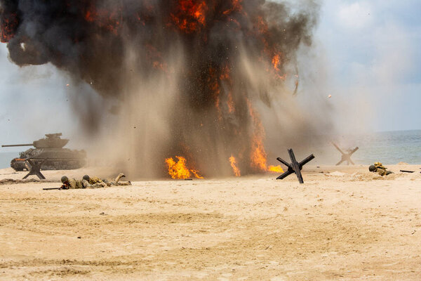 Историческая реконструкция Второй мировой войны. Поле боя. Взрывы, танк и американские солдаты на пляже. Дым и пыль.