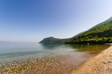 Ohri Gölü. Ljubanista köyünün yakınındaki resim gibi bir sahil şeridi. Mavi göl, altın plaj ve ağaçlarla kaplı yeşil dağlar. Makedonya Cumhuriyeti