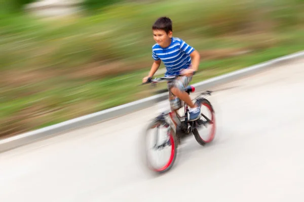 都会の公園で高速で自転車に乗っている男の子の動きのぼかしイメージ — ストック写真