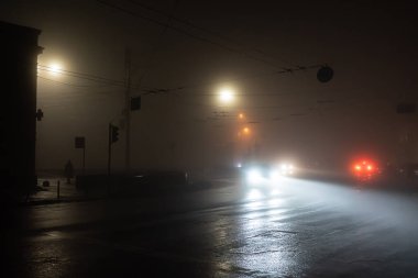 Elektrik kesintisi sırasında Ukrayna 'nın başkenti Kyiv' in sokakları sisli havada tamamen karanlık yerleşim alanlarının arka planına karşı geçen arabaların ışıkları ve yalnız sokak lambalarıyla aydınlanıyor..
