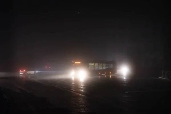 ウクライナの首都キエフの完全に暗い通りは 停電中の霧の中で夜に通過車のライトによって照明されています — ストック写真