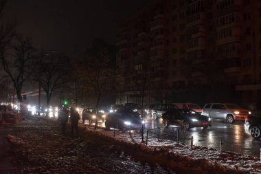KYIV, UKRAINE - 16 Aralık 2022 Kyiv 'deki elektrik kesintisi sırasında karanlık binalar. Araba farlarının ışığında, yoldan geçenler karla kaplı bir kaldırımda görülebilir..