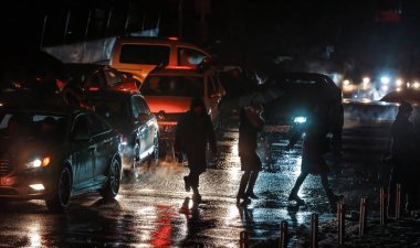 KYIV, UKRAINE - 16 Aralık 2022: Yoldan geçenler araba farlarıyla aydınlatılmış yaya geçidinde karşıdan karşıya geçiyorlar. Kyiv 'deki elektrik kesintisi sırasında ışıksız karanlık binalar.