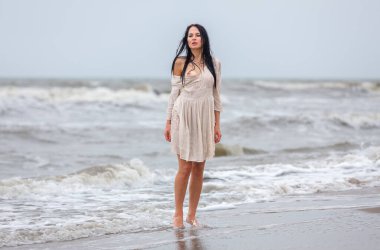 Beautiful young seminude woman in the cold sea waves. Emotional woman in a white dress worn on her bare body enjoying the coolness of the cold sea.