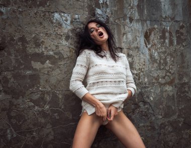 An emotional young woman in a white wool sweater poses against a concrete wall