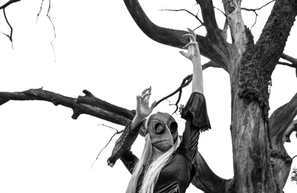 Natures beauty with a touch of mystery. A mystical and captivating image - a blonde woman in a crow mask posing near a dry tree, creating an aura of mystery and beauty. Black and white image