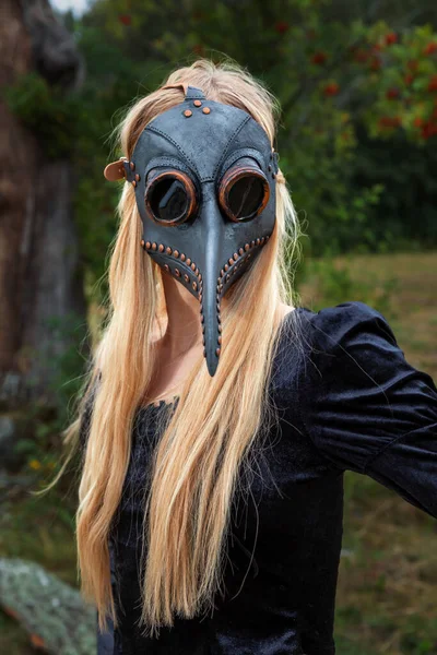 Natures beauty with a touch of mystery. A mystical and captivating image - a blonde woman in a crow mask posing near a withered tree in nature, creating an aura of mystery and beauty.